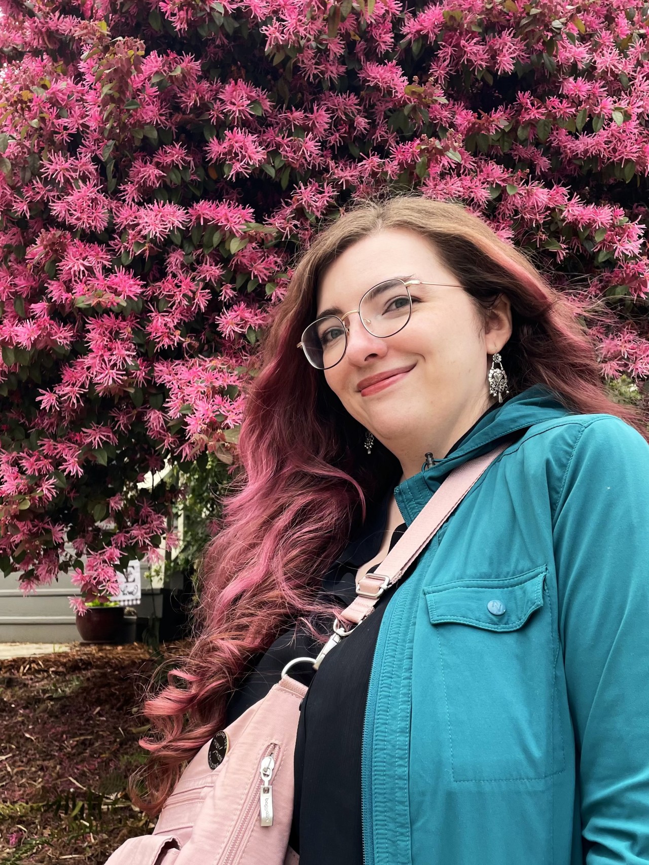 Tulip, as in the person writing this, smiling in front of a pink flowering tree. their hair matches the color of the flowers