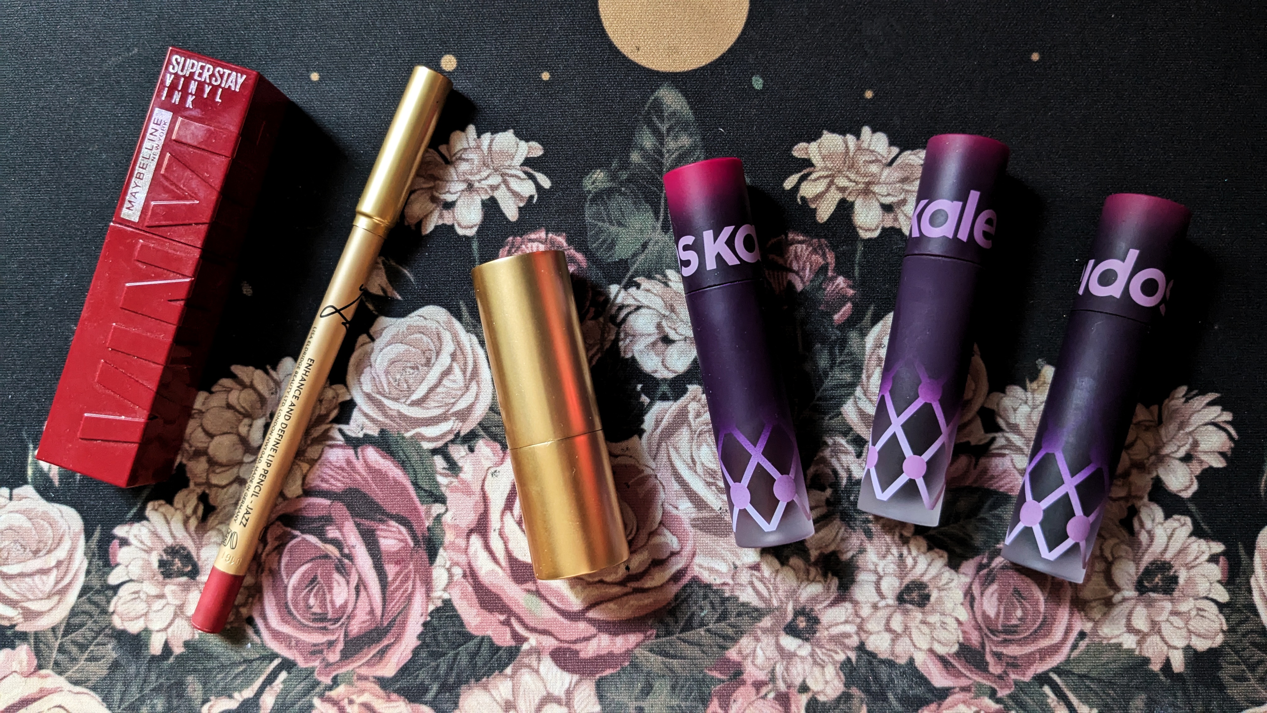 photo: several lipsticks laid out on a desk, with a dark, floral background behind them.